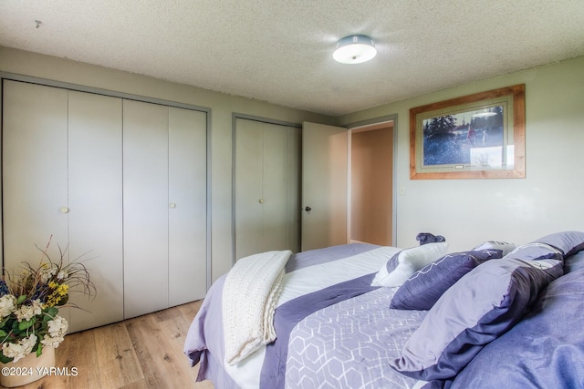 bedroom with light wood-style floors, a textured ceiling, and multiple closets