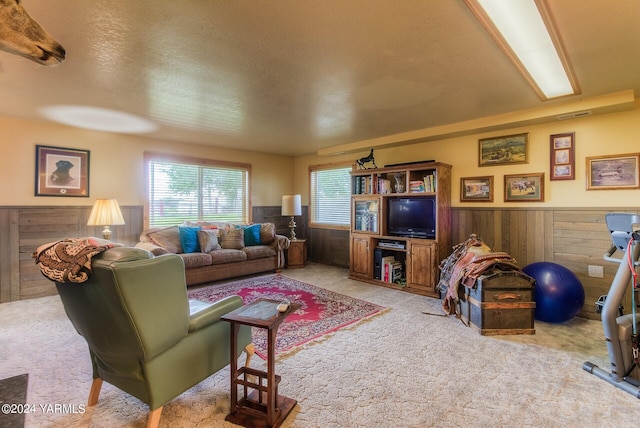 living area featuring a textured ceiling, light carpet, wood walls, visible vents, and wainscoting