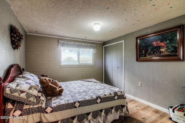 bedroom featuring baseboards, a textured wall, a textured ceiling, light wood-type flooring, and a closet