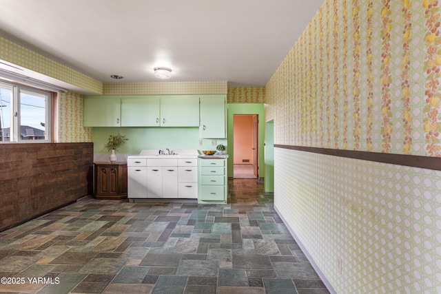 kitchen with wallpapered walls, light countertops, green cabinetry, and a sink