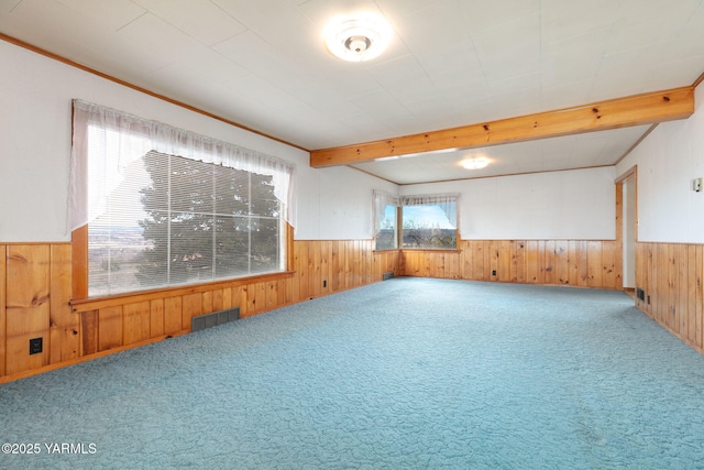 empty room featuring a wainscoted wall, visible vents, beamed ceiling, and wooden walls