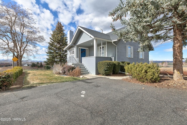 view of front of property featuring covered porch, a chimney, and a front yard