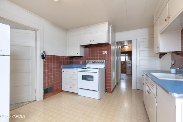 kitchen with white appliances, a sink, tile walls, white cabinets, and light floors