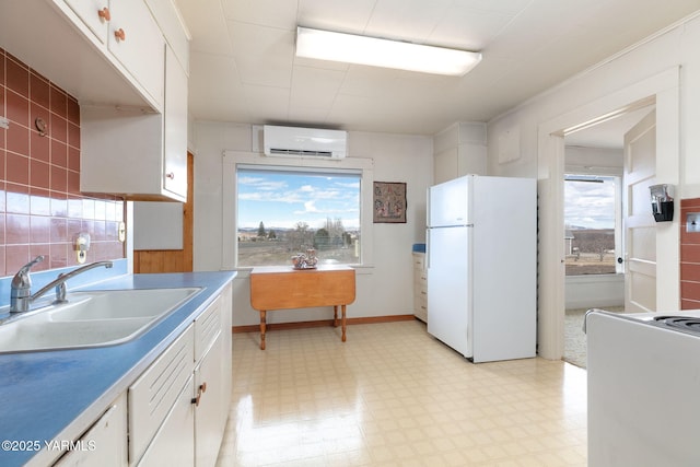 kitchen featuring light floors, freestanding refrigerator, white cabinetry, a sink, and a wall mounted air conditioner