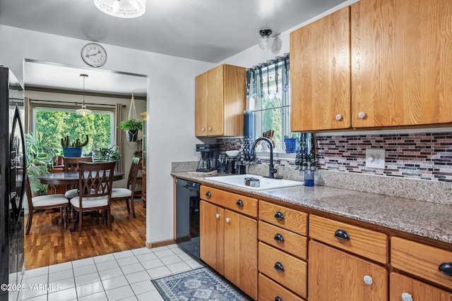 kitchen with brown cabinets, a sink, light tile patterned floors, backsplash, and black appliances