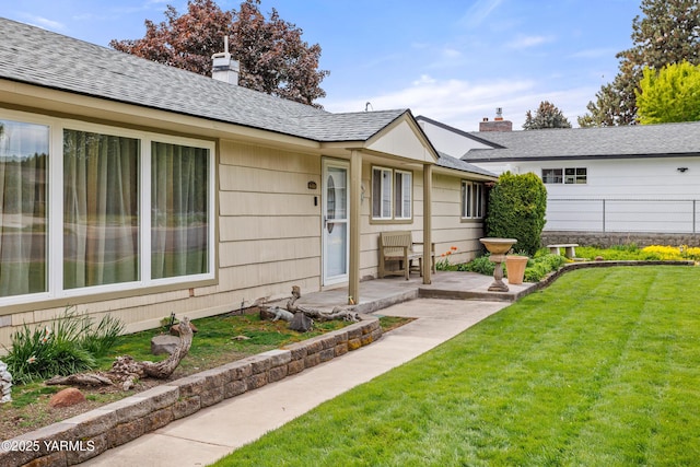 view of front of house with fence, roof with shingles, a front lawn, a chimney, and a patio