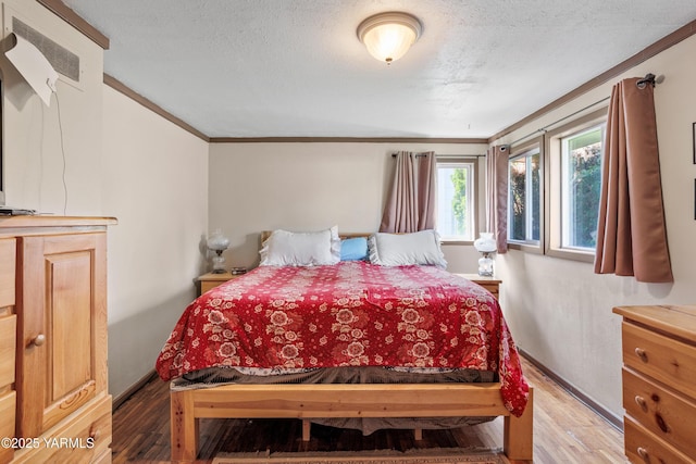 bedroom with crown molding, a textured ceiling, baseboards, and wood finished floors