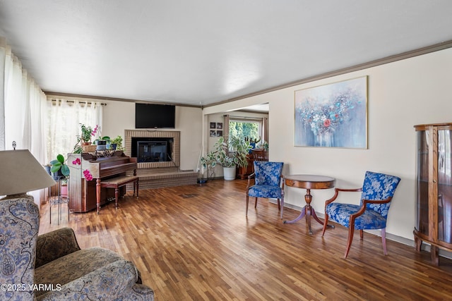 living area with crown molding, baseboards, a fireplace, and wood finished floors