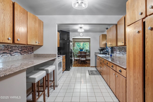 kitchen featuring a breakfast bar area, backsplash, brown cabinets, light tile patterned floors, and freestanding refrigerator