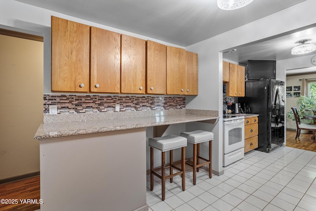 kitchen featuring decorative backsplash, a kitchen breakfast bar, white electric stove, light tile patterned floors, and black fridge