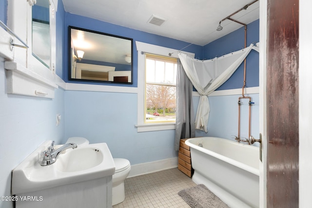 bathroom with a freestanding tub, tile patterned floors, toilet, visible vents, and a sink