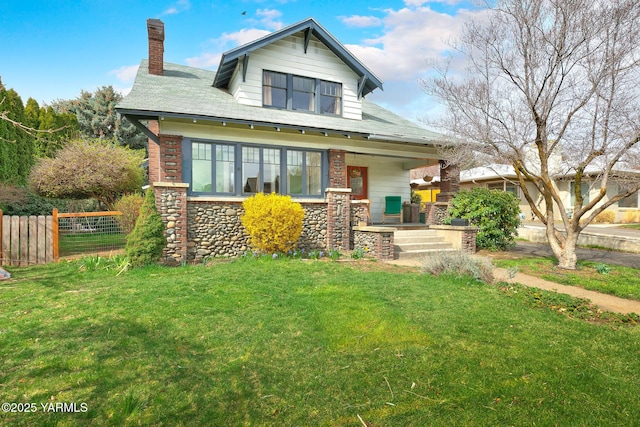 view of front of property with covered porch, stone siding, fence, a front lawn, and a chimney