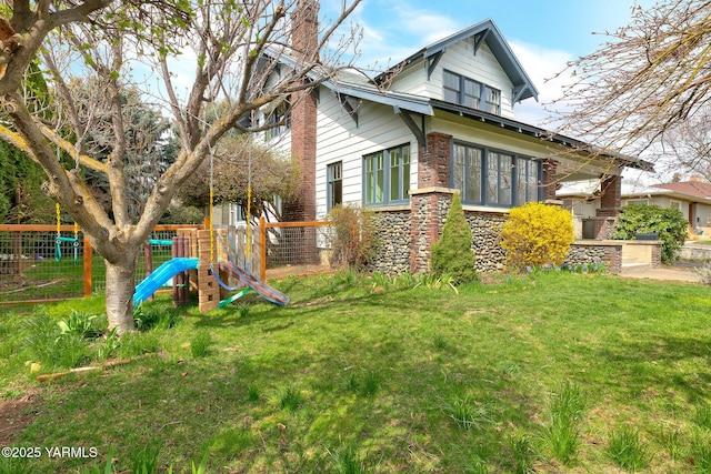 view of side of property featuring stone siding, fence, a playground, and a lawn