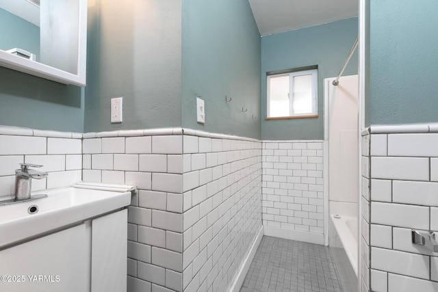 bathroom featuring tile patterned floors, vanity, wainscoting, and tile walls