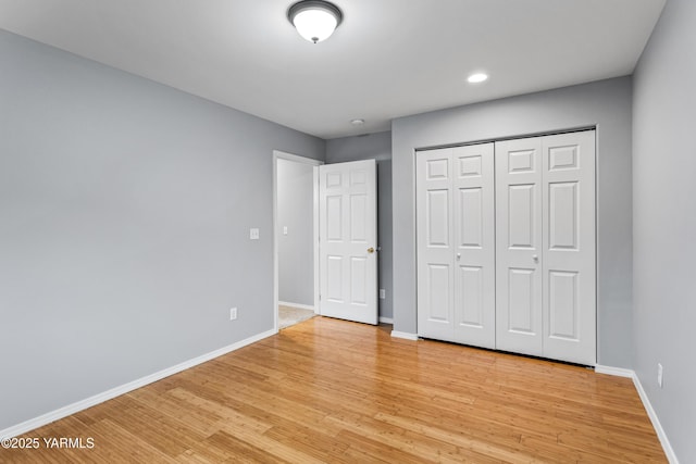 unfurnished bedroom featuring light wood-style flooring, baseboards, and a closet