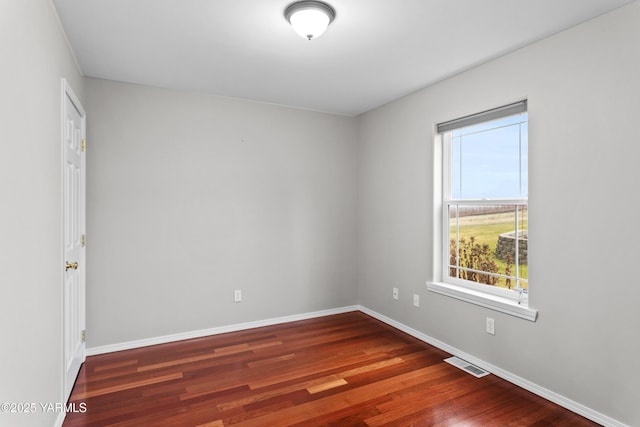 empty room with visible vents, dark wood finished floors, and baseboards