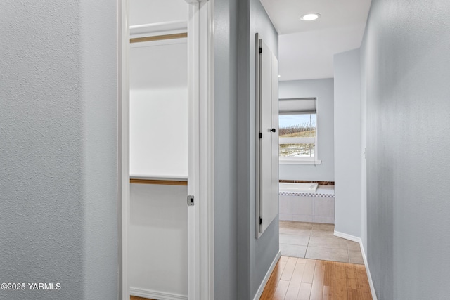 hall featuring light wood finished floors, baseboards, and a textured wall