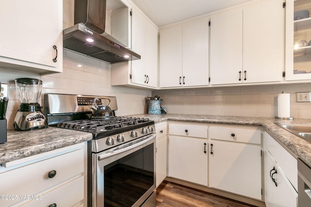 kitchen with wall chimney range hood, stainless steel gas range oven, and white cabinets