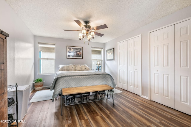 bedroom featuring multiple closets, baseboards, a textured ceiling, and wood finished floors
