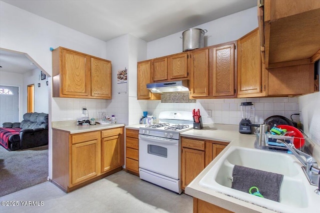 kitchen featuring brown cabinetry, gas range gas stove, light countertops, under cabinet range hood, and a sink