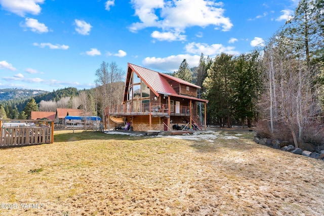 back of property featuring a deck, metal roof, stairs, a lawn, and a view of trees