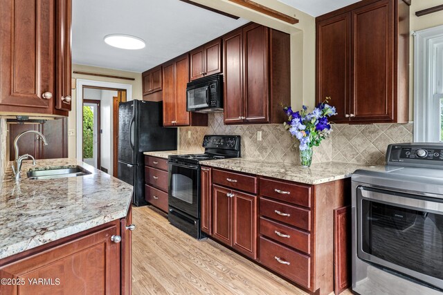 kitchen with washer / clothes dryer, black appliances, a sink, light wood-type flooring, and light stone countertops