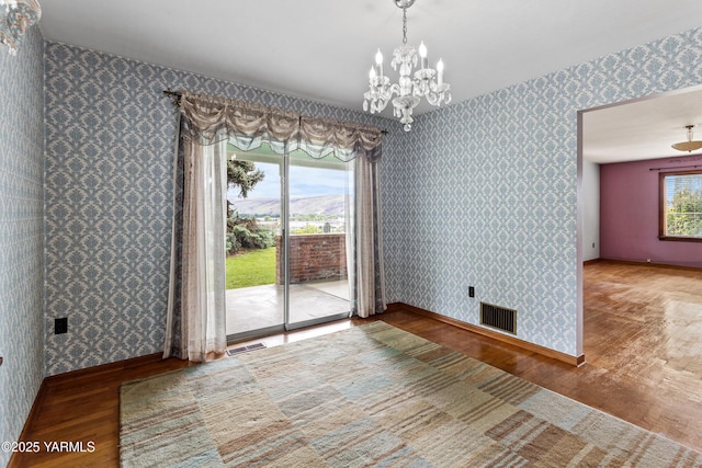 unfurnished dining area with wallpapered walls, wood finished floors, a chandelier, and baseboards