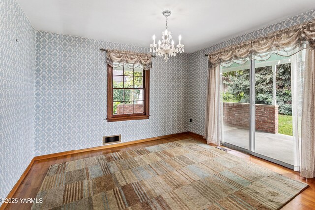 unfurnished dining area with wallpapered walls, wood finished floors, and a chandelier