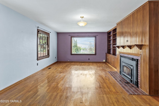 unfurnished living room featuring light wood finished floors, plenty of natural light, a fireplace with flush hearth, and baseboards