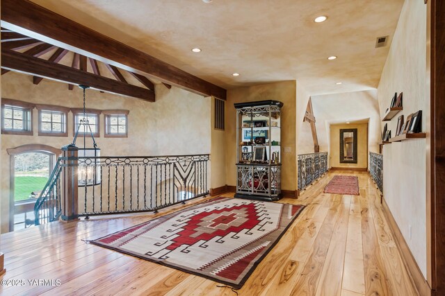 hall featuring visible vents, beamed ceiling, an inviting chandelier, and wood finished floors