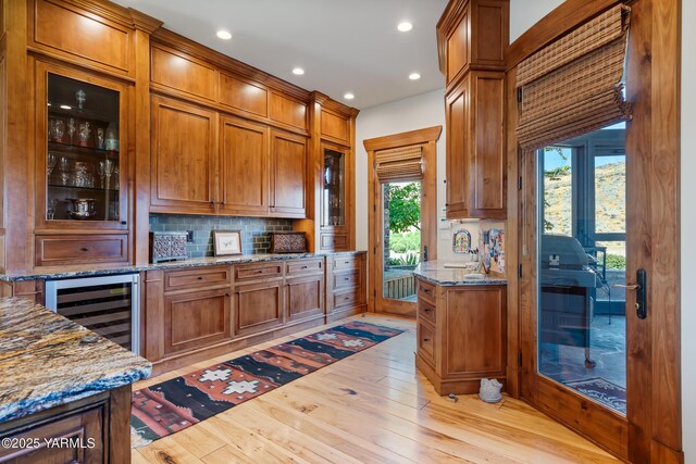 kitchen with wine cooler, light stone counters, and brown cabinets