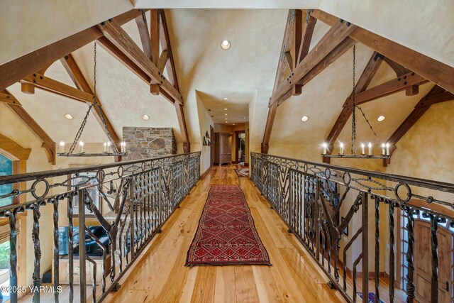 hall with high vaulted ceiling, beamed ceiling, wood finished floors, and an inviting chandelier