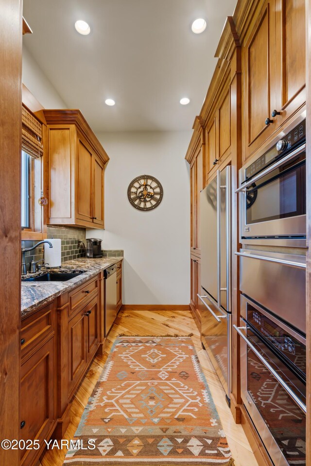 kitchen featuring stainless steel appliances, brown cabinetry, a sink, and light stone counters