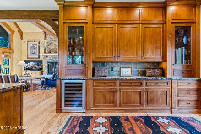 kitchen with light stone counters, wine cooler, tasteful backsplash, light wood-style floors, and beamed ceiling