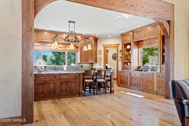 kitchen featuring arched walkways, hanging light fixtures, brown cabinetry, a healthy amount of sunlight, and light wood-type flooring