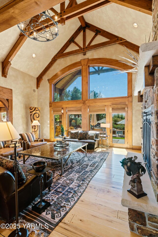 living room with high vaulted ceiling, a stone fireplace, beamed ceiling, and light wood-type flooring