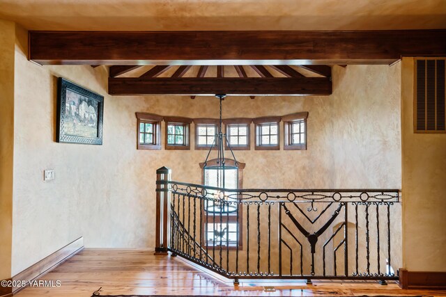 hallway featuring a textured wall, wood finished floors, beam ceiling, an upstairs landing, and a notable chandelier