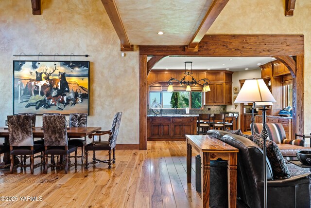 dining area featuring arched walkways, beam ceiling, a textured wall, light wood-style floors, and baseboards