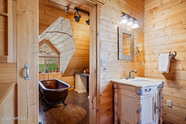 full bath with a freestanding tub, wooden walls, vanity, and wood finished floors