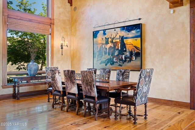 dining space featuring a high ceiling, light wood-style flooring, and baseboards