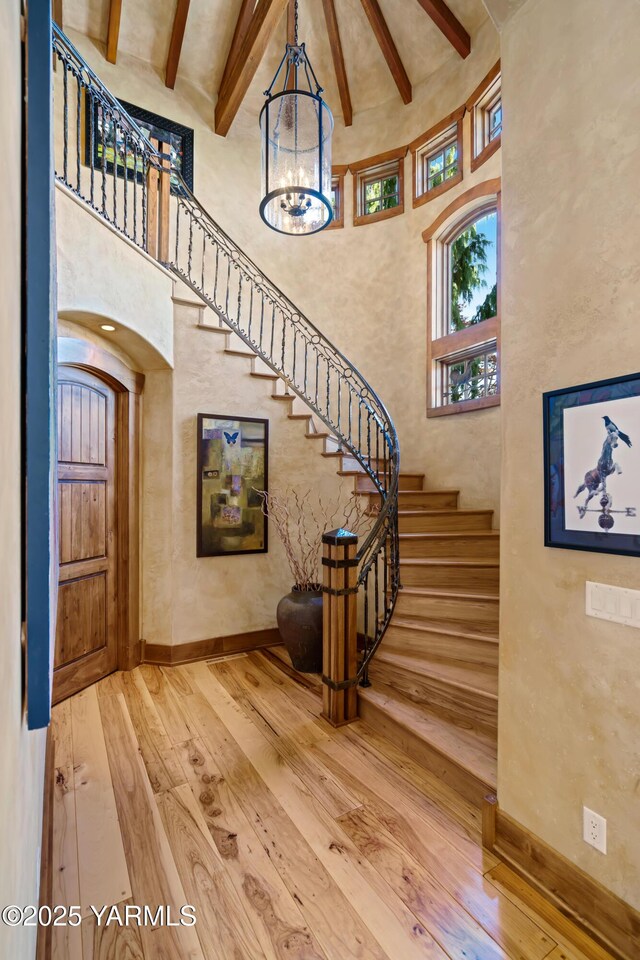 entryway featuring a towering ceiling, arched walkways, beamed ceiling, and wood finished floors