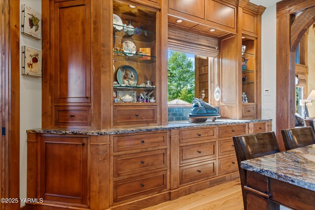 kitchen with stone counters, arched walkways, built in features, brown cabinetry, and light wood-style floors