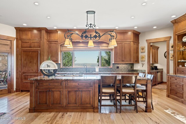 kitchen with stone counters, a center island, brown cabinets, light wood finished floors, and pendant lighting