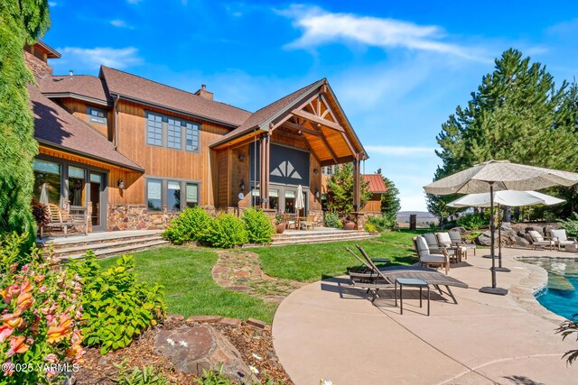 back of house featuring stone siding, a yard, a chimney, and a patio area