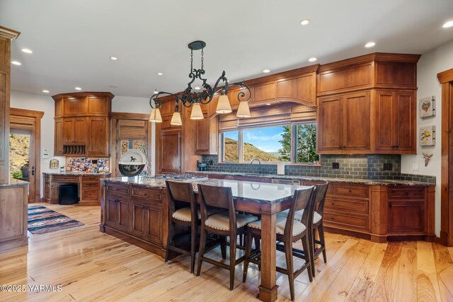 kitchen with stone countertops, a kitchen island, light wood-style floors, backsplash, and decorative light fixtures