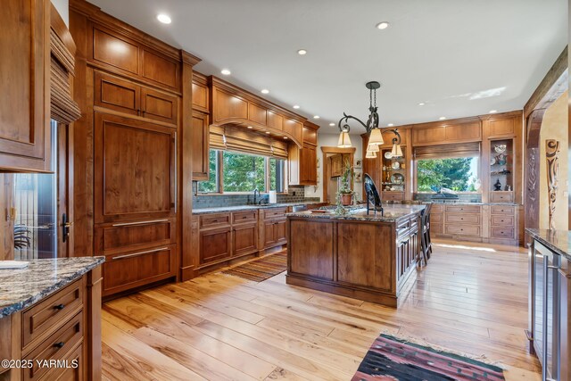 kitchen featuring dark stone counters, an island with sink, a sink, and decorative light fixtures