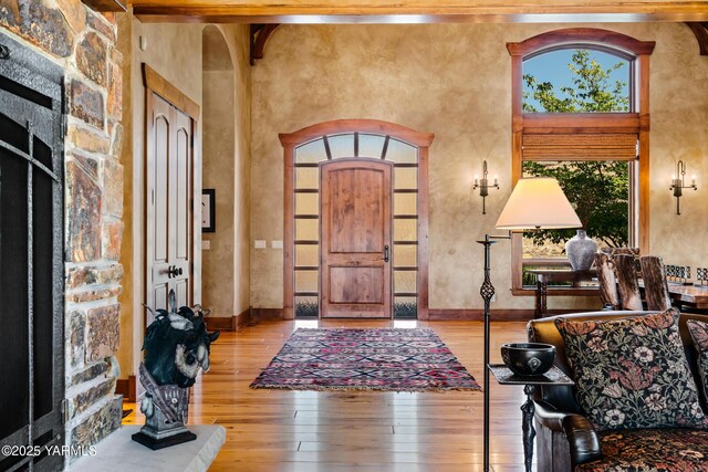 entryway with arched walkways, wood finished floors, a towering ceiling, baseboards, and beam ceiling