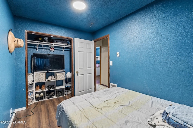 bedroom with visible vents, a closet, wood finished floors, and a textured wall