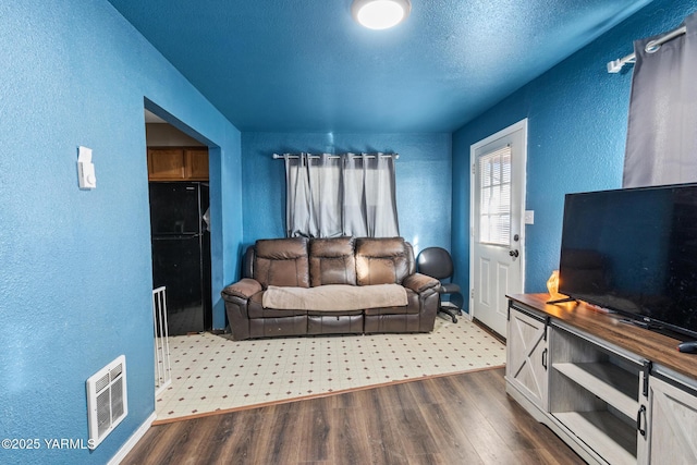 living area featuring wood finished floors, visible vents, a textured wall, and a textured ceiling