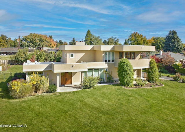 rear view of house featuring a balcony, fence, a lawn, and stucco siding